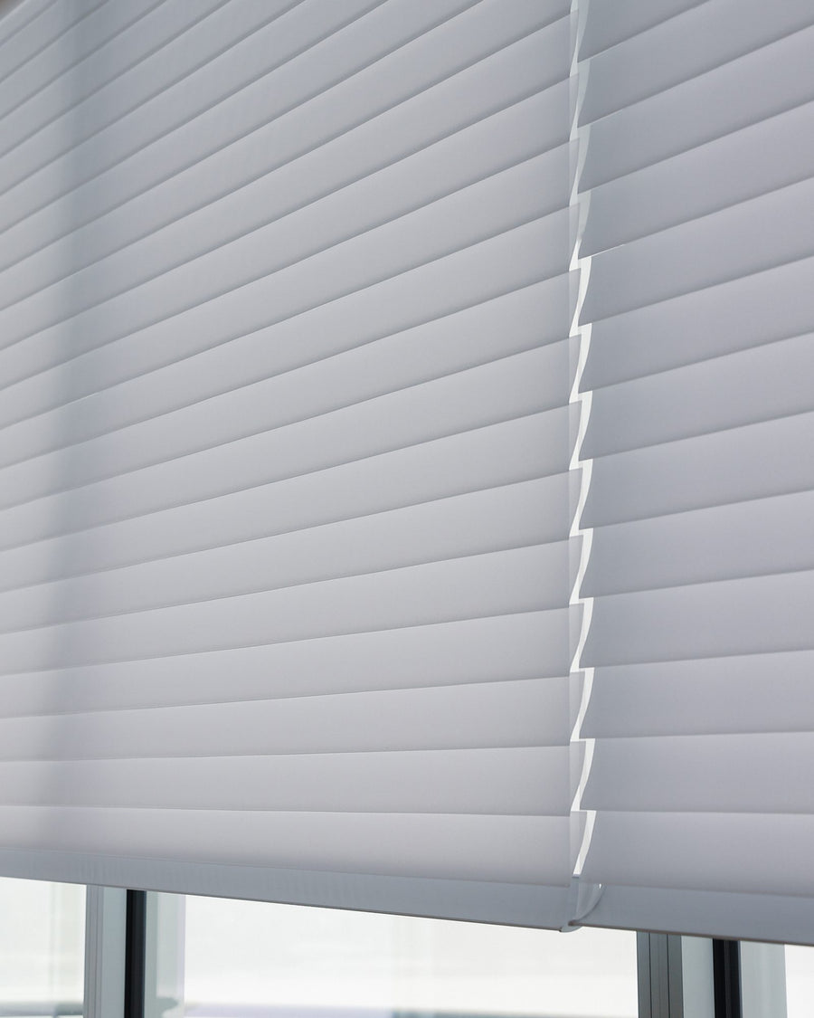 A white sheer shade lowered across a tall window, daylight coming softly through the fabric